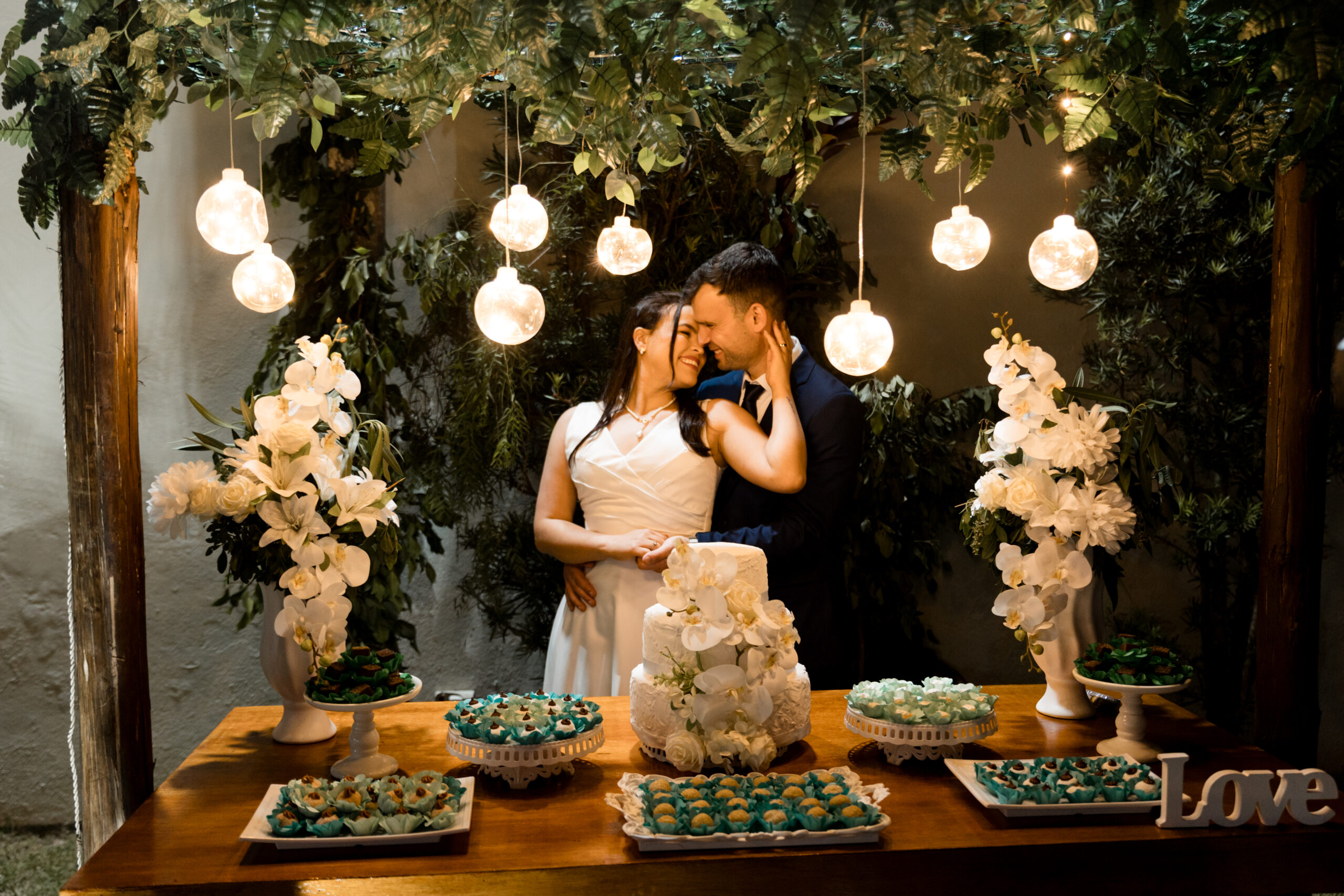 Casal de noivos em frente a uma mesa de doces iluminada