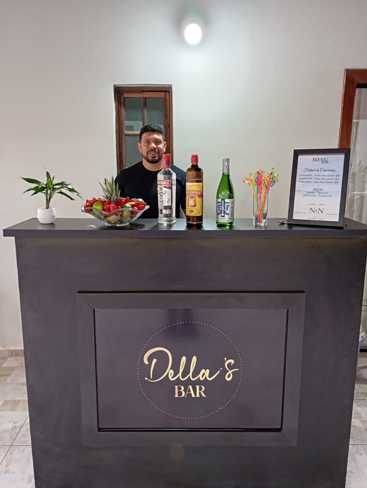 Bartender do Della's Bar posando atrás do balcão de bar móvel com equipamentos e frutas